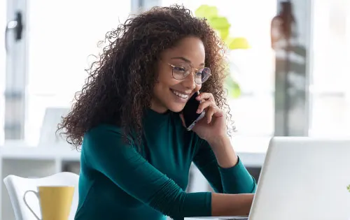 Person smiling while chatting on the phone in front of laptop. 