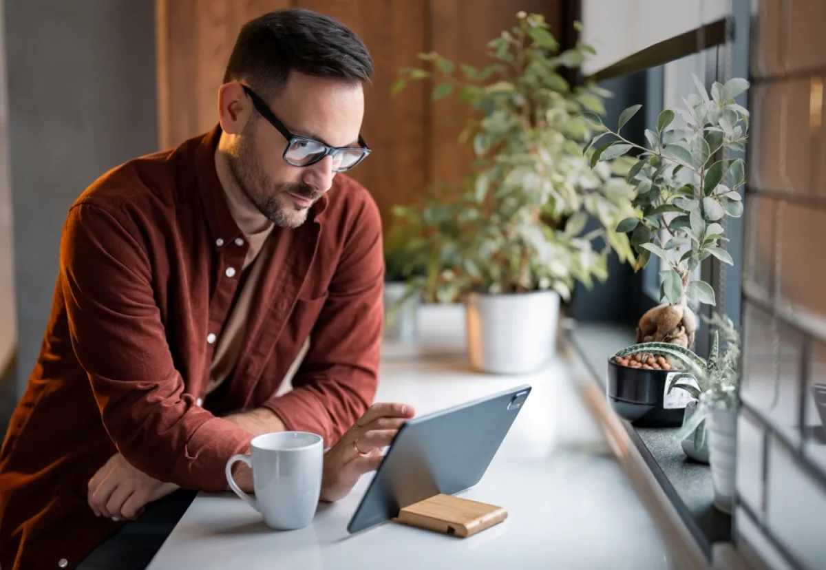 Image of a young, male sole trader in a stylish kitchen, drinking a coffee while working off his tablet.