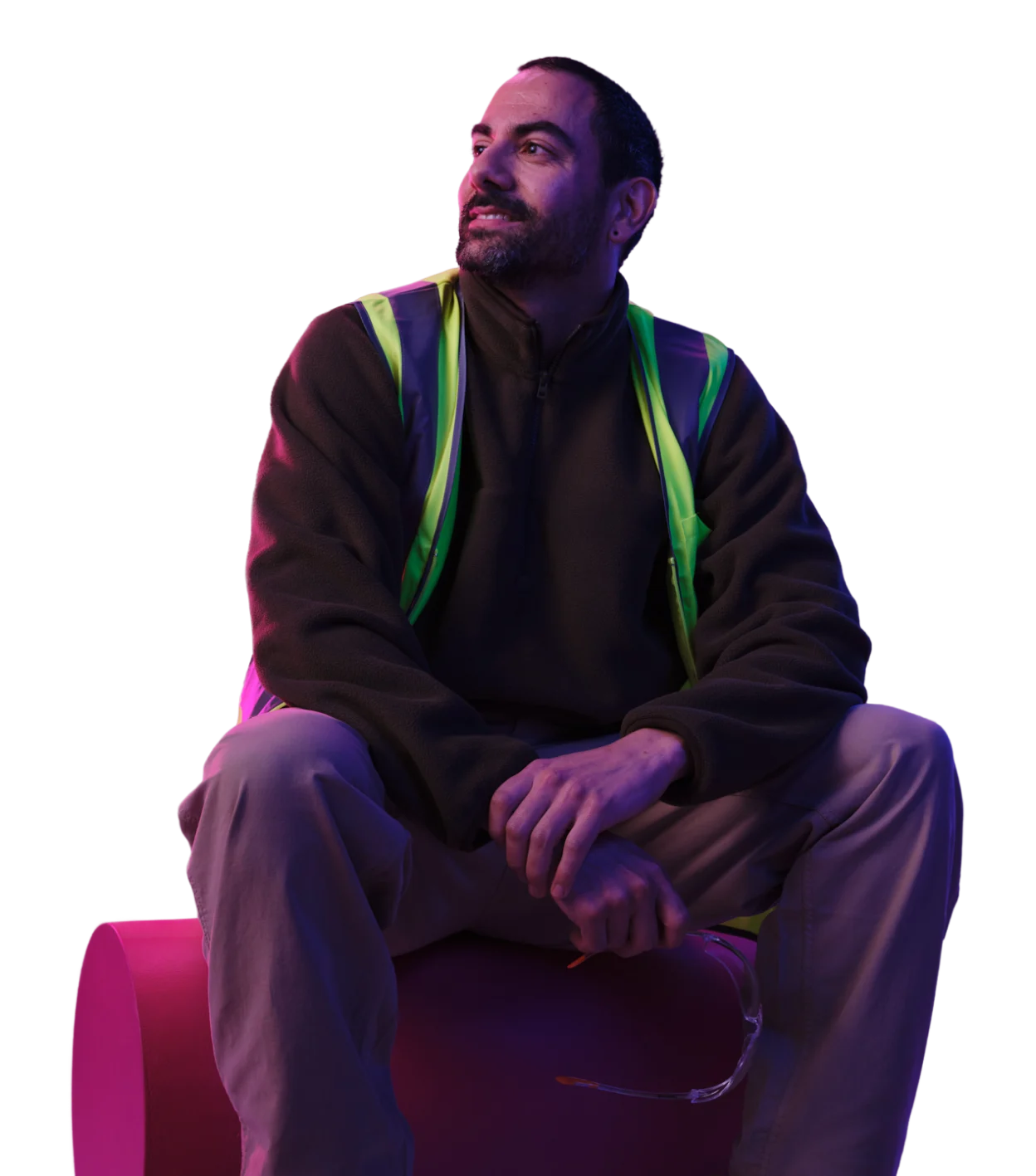 Person in dark jacket with reflective safety vest sitting under colorful purple and pink lighting.