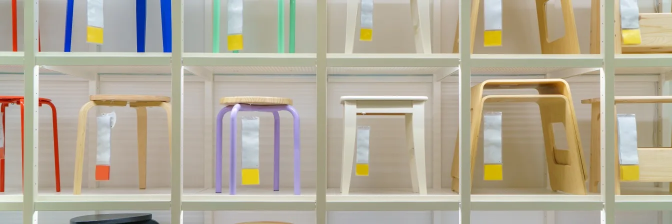 Modern wooden stools in various colors displayed on white shelving, including purple, red, white, and natural wood designs.
