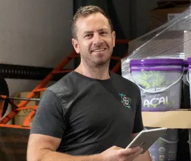General Manager of The Berry Man, Greg O'Toole, standing in front of a pallet of acai berry products.