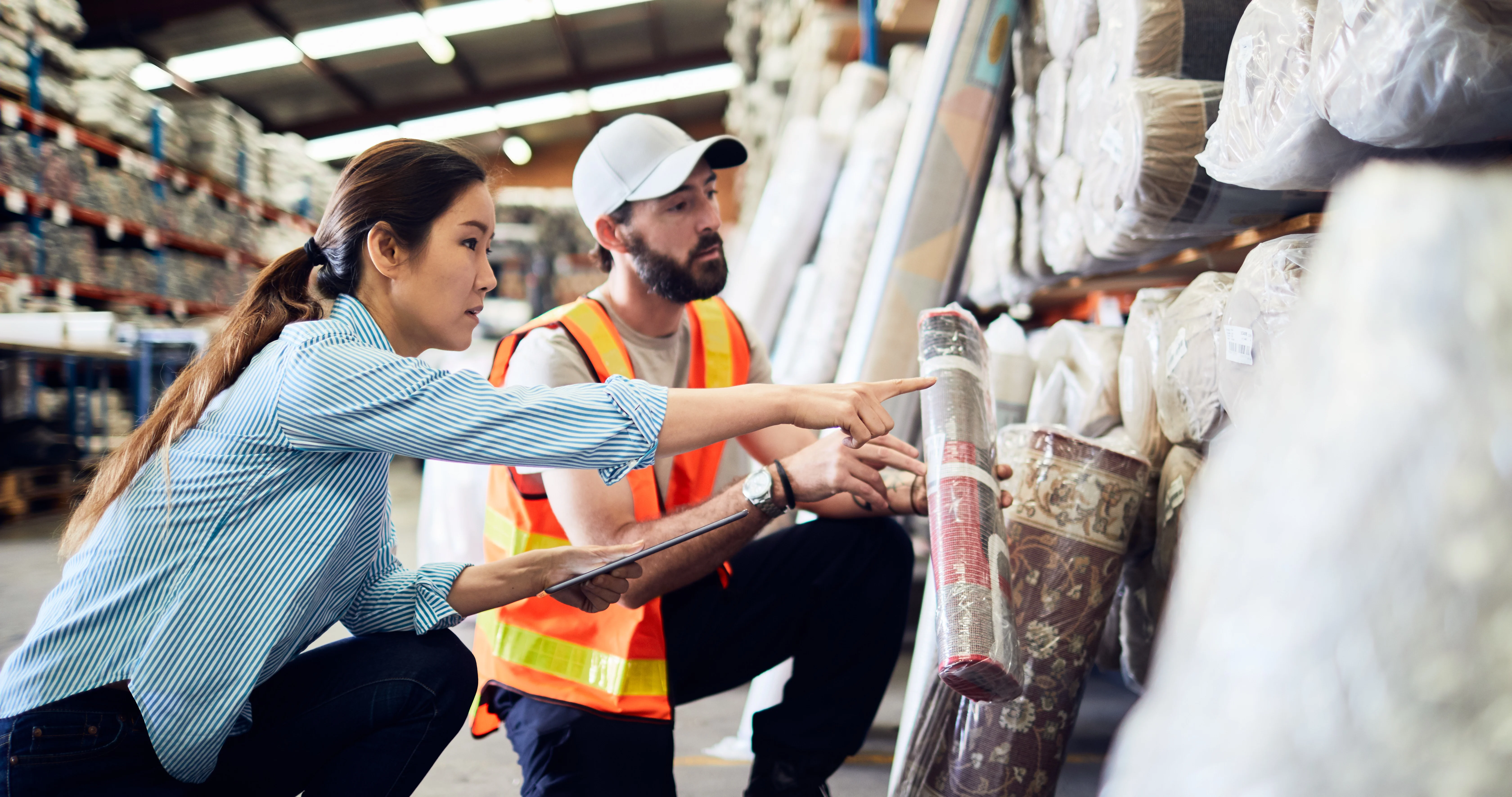 Two workers in a warehouse checking inventory of floor rugs