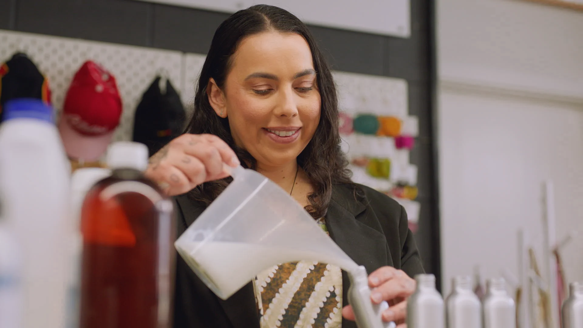 Person in dark jacket, smiling while pouring a white liquid into a container.