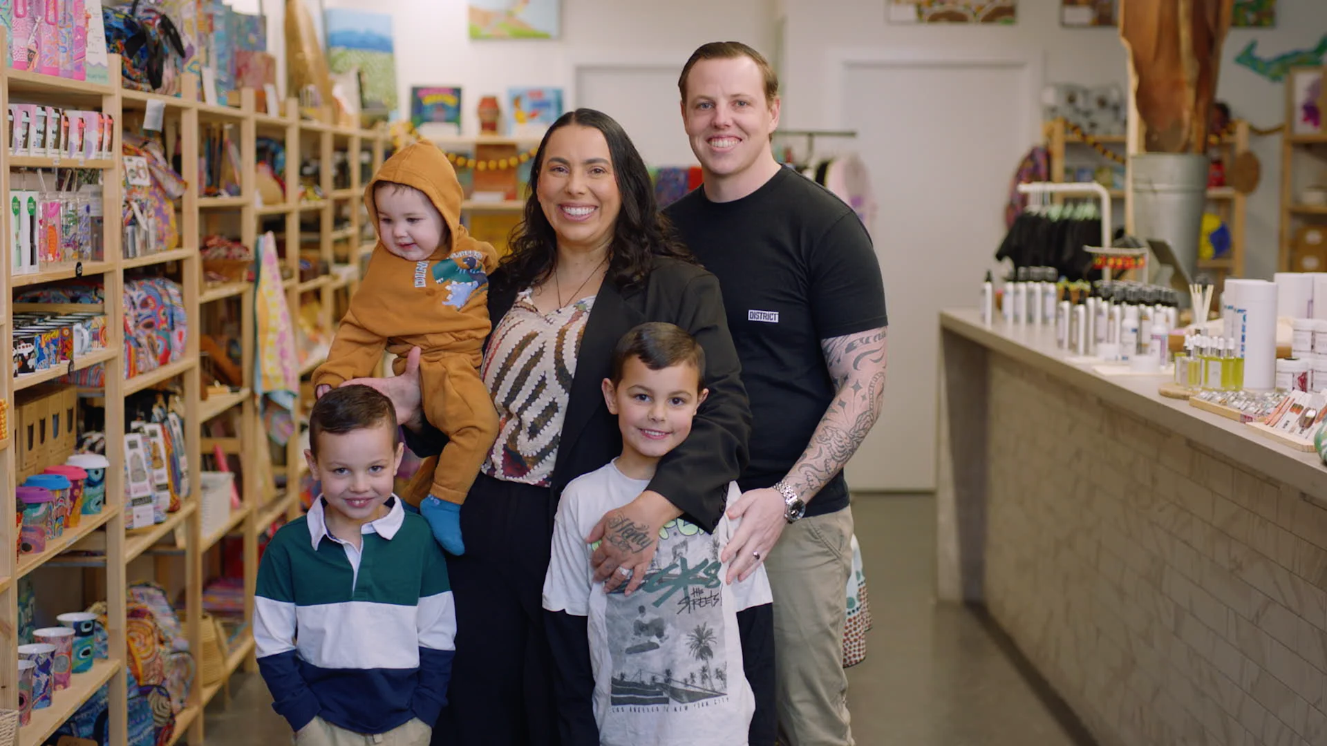 Family of five posing together in a colorful retail shop with wooden shelves of merchandise and display counter.
