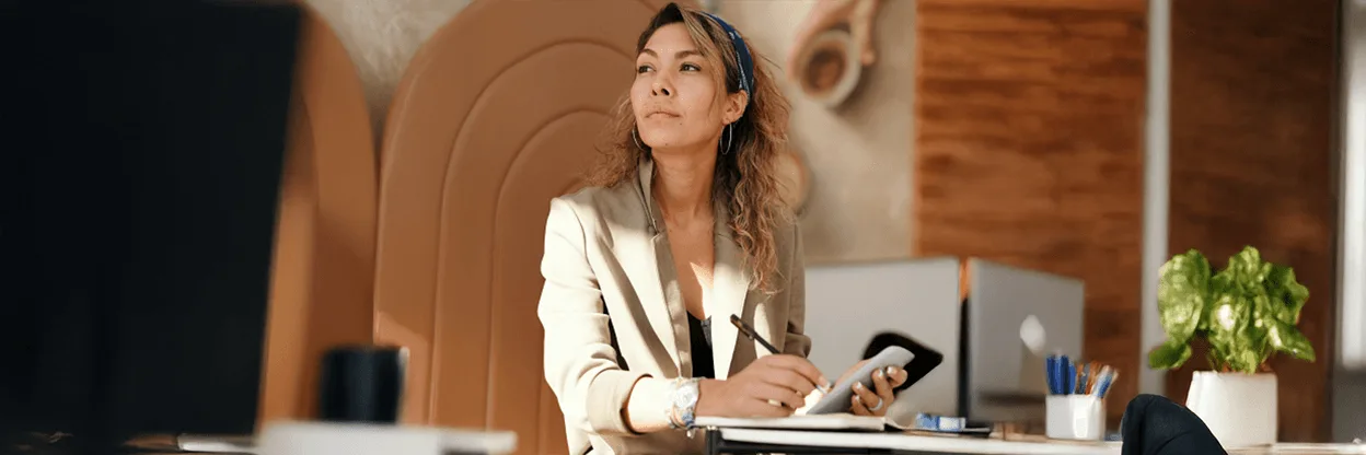 Person in cream blazer writing notes in modern office with warm wood panels and arched wall design.