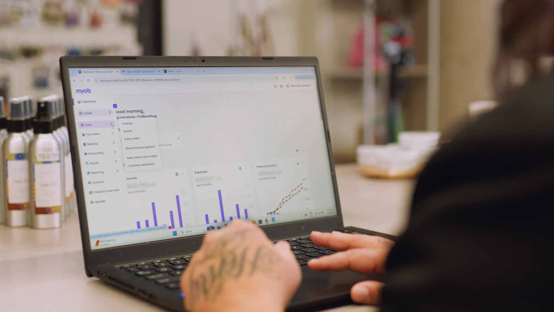 Person using MYOB accounting software on laptop, viewing financial dashboard with purple bar graphs and charts.