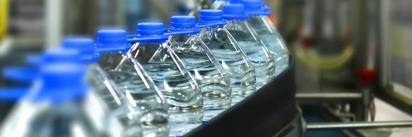 Row of plastic water bottles with bright blue caps on a production line in a bottling facility.