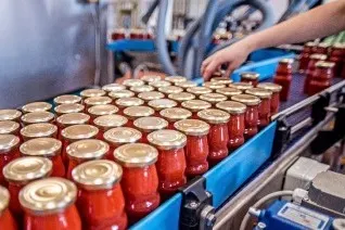 Rows of sealed red jars on a food production line with a worker's hand visible in a processing facility.