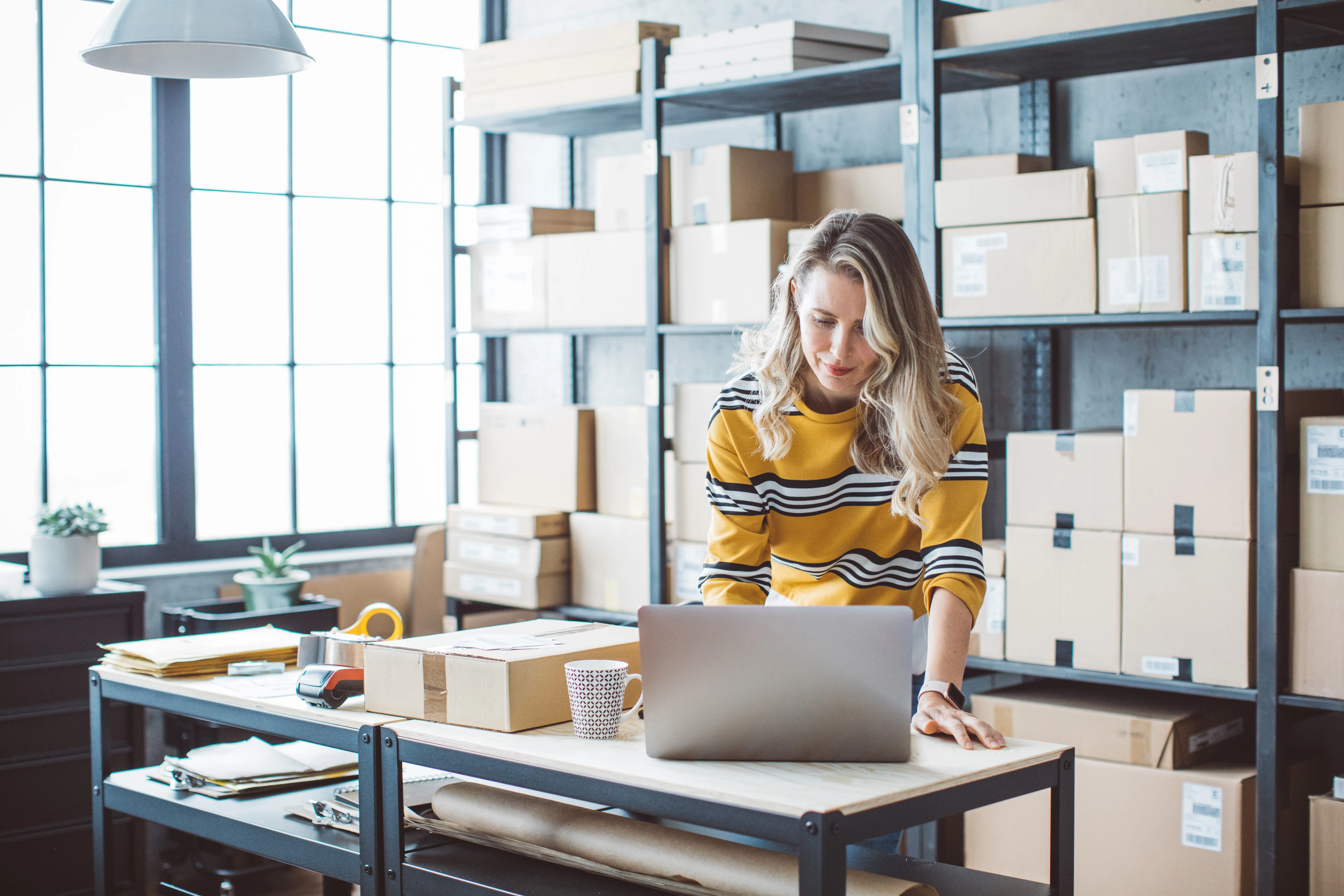 Business woman using her laptop, surrounded by boxes of inventory.