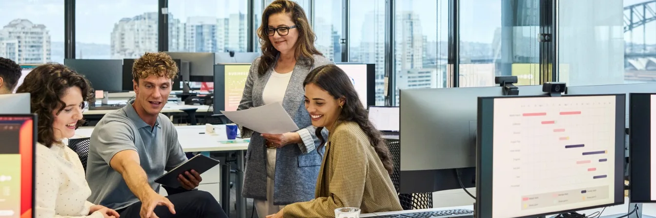Team collaborating in modern office with city skyline view through glass windows, project timeline visible on screen.