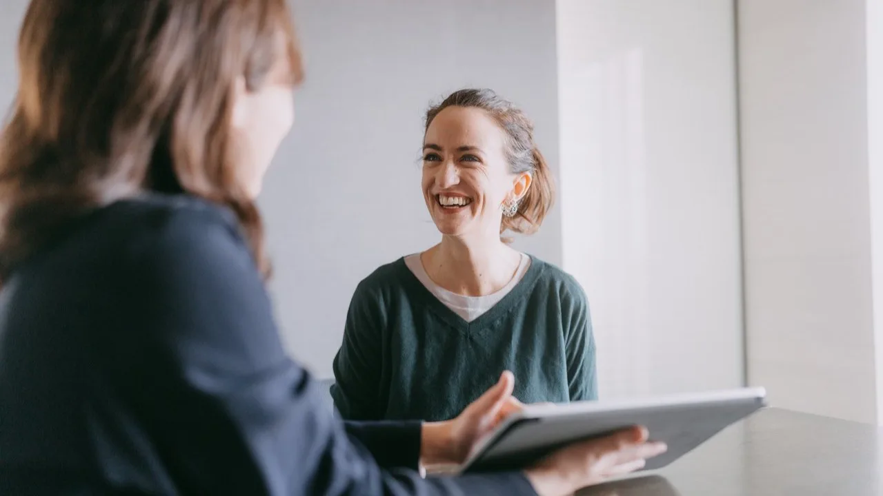 A woman meets with an advisor to discuss professional matters, smiling as they review information on a tablet.