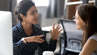 Employer in corporate attire talks to employee in an office.