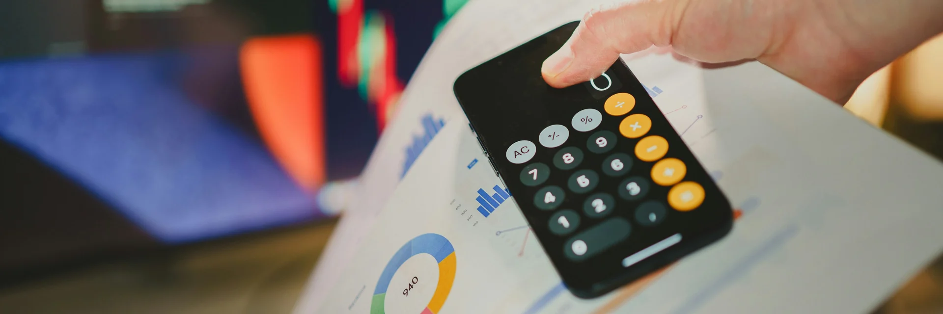A person holding a mobile phone with the calcular app on the screen on top of a financial report print out.