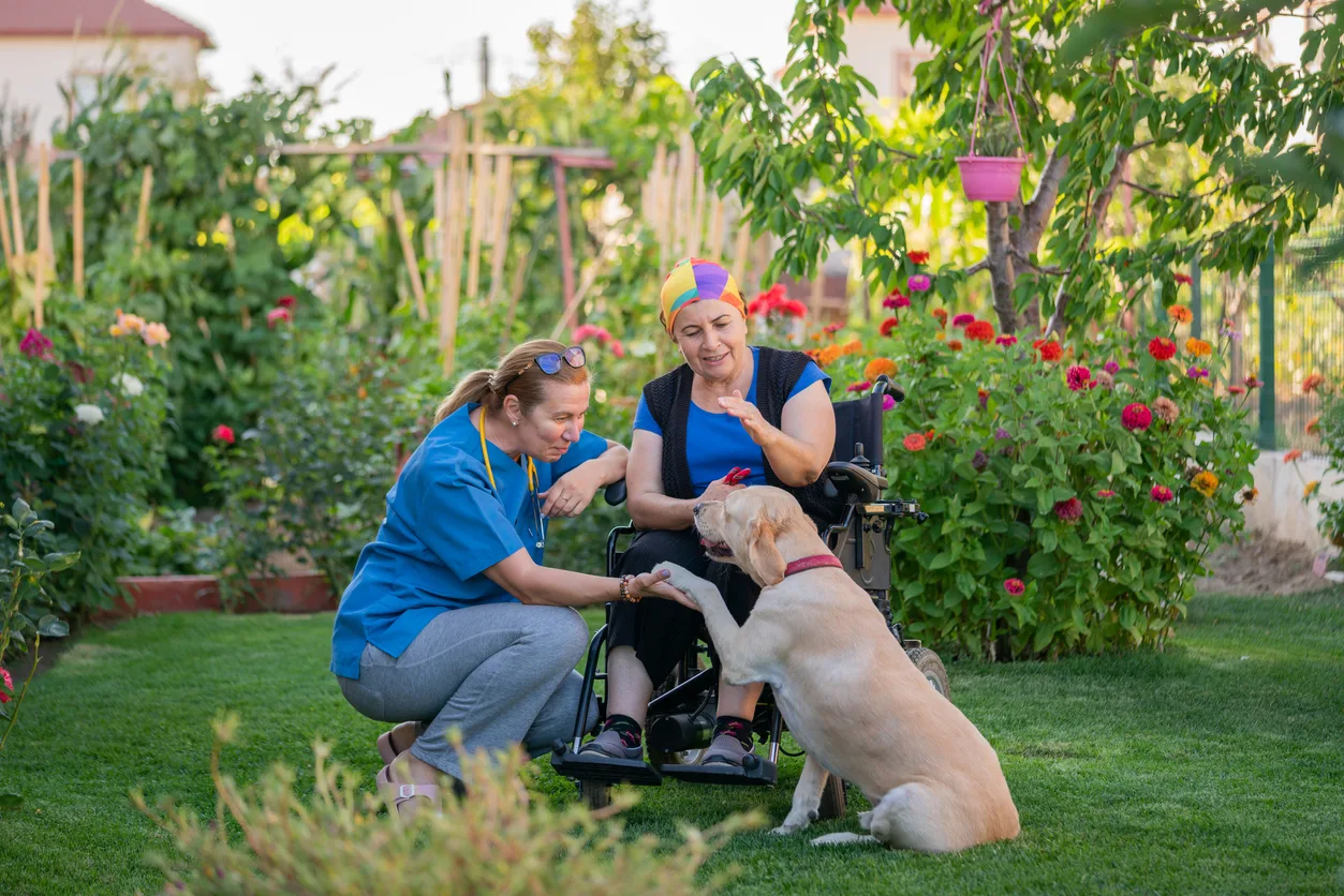 woman-with-disability-in-garden-with-caregiver-and-dog