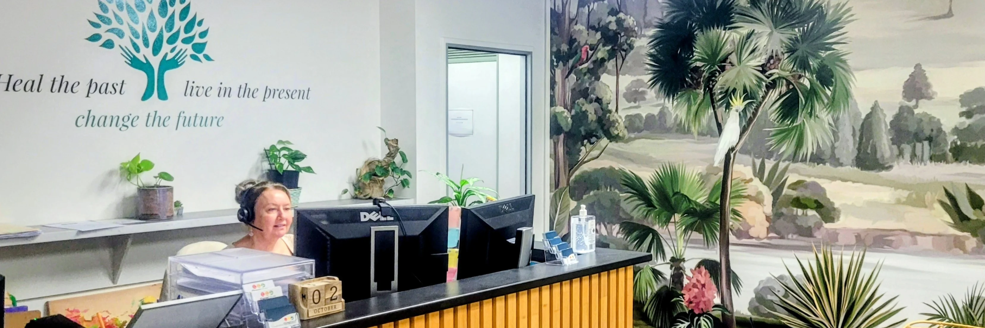 Reception desk with tropical mural, tree logo, and inspirational quote "Heal the past, live in the present, change the future"