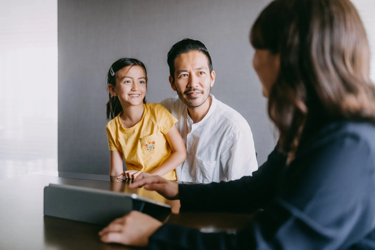 A child in yellow shirt and adult in white shirt smiling during a meeting with a professional holding a tablet.