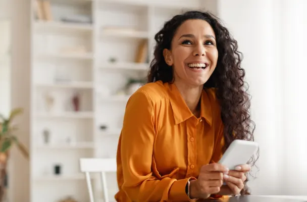 A woman in an orange shirt holding a mobile phone and smiling