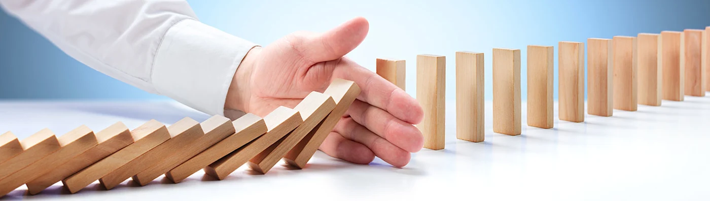 Hand blocks a line of standing jenga blocks from all falling down