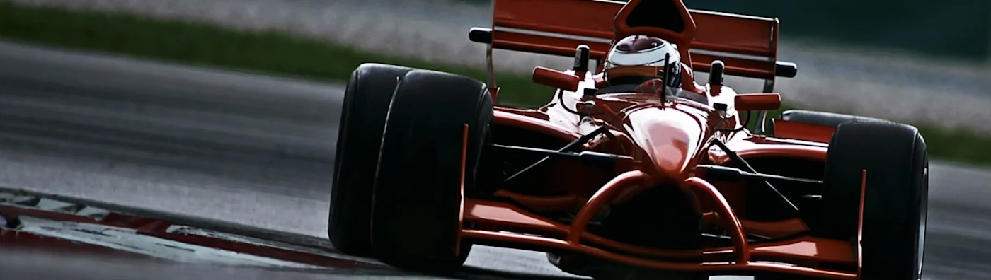 Red race car speeds around a track, driven by a helmeted racer in full gear.