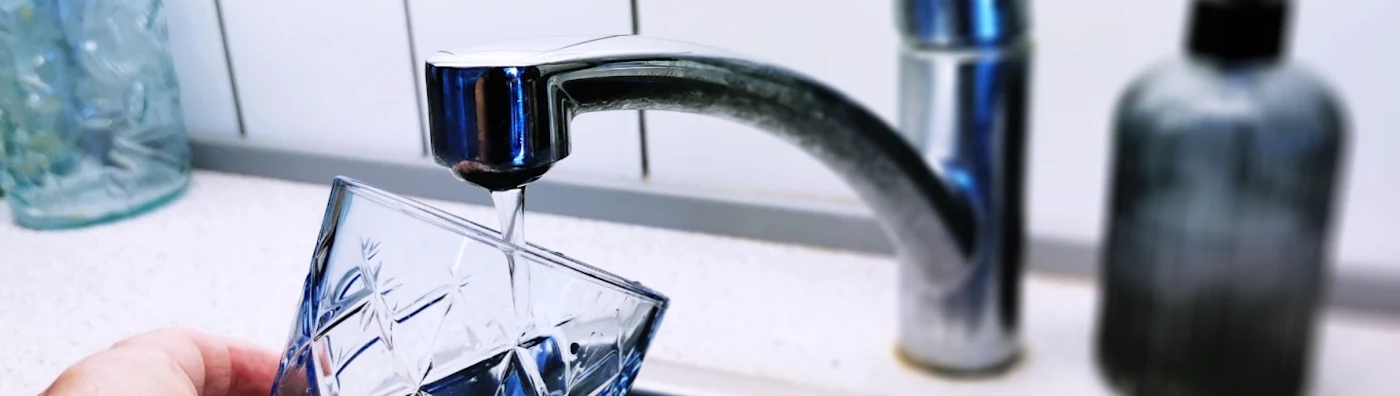 Person pouring drinking water from the tap into a glass 
