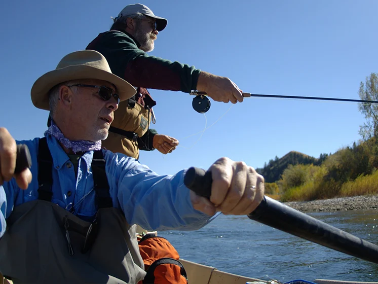 Close up image of two men fly fishing on a sunny day, casting a line.