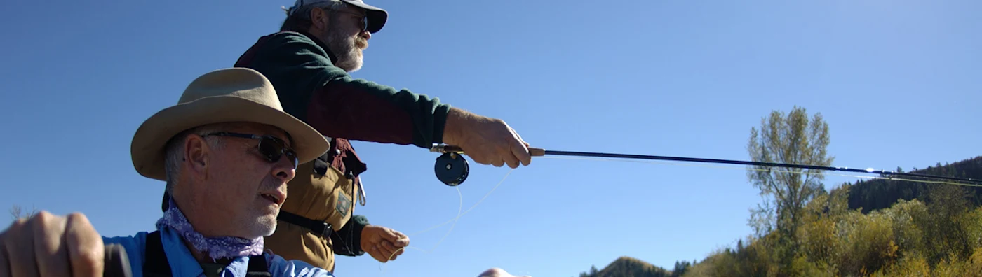 Close up image of two men fly fishing on a sunny day, casting a line.