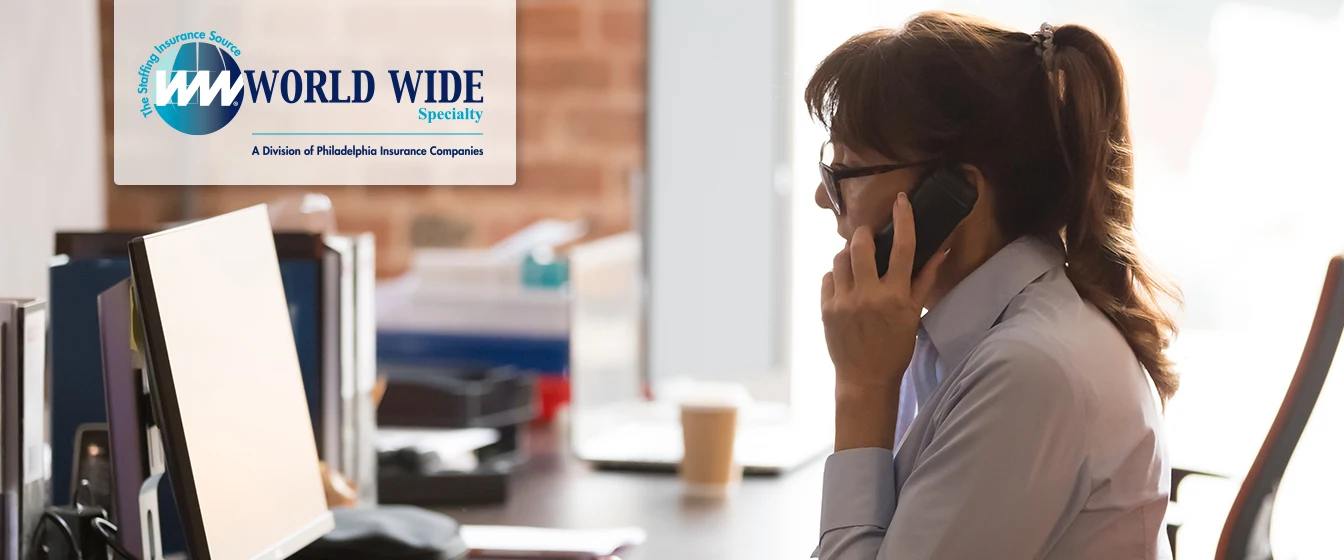 A female temporary office worker multitasking between a phone call and her computer. World Wide Specialty text and logo accompanies image