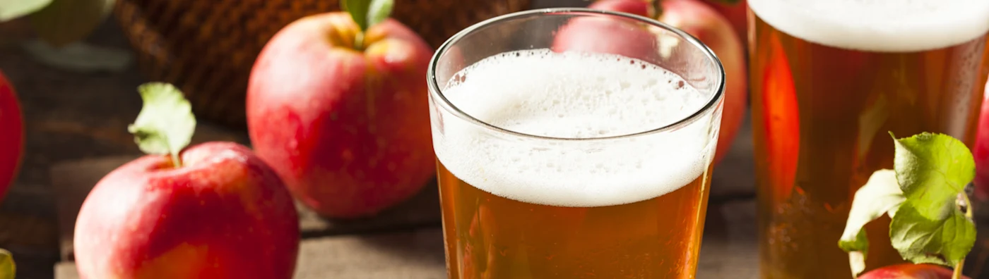 Tall glass of hard apple cider surrounded by apples, ready to drink.