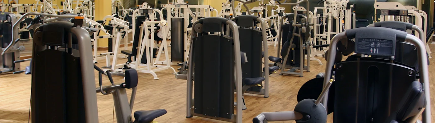 Gym filled with various weight machines and exercise equipment on a wooden floor.
