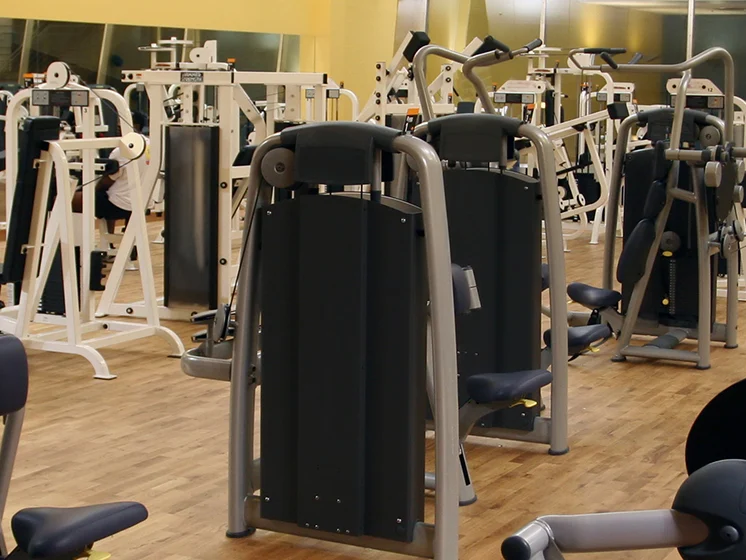 Gym filled with various weight machines and exercise equipment on a wooden floor.