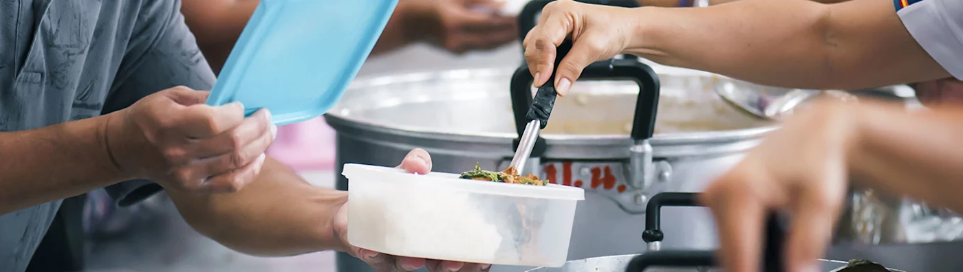 Image shows Food service in a soup kitchen (image shows hands only no faces)