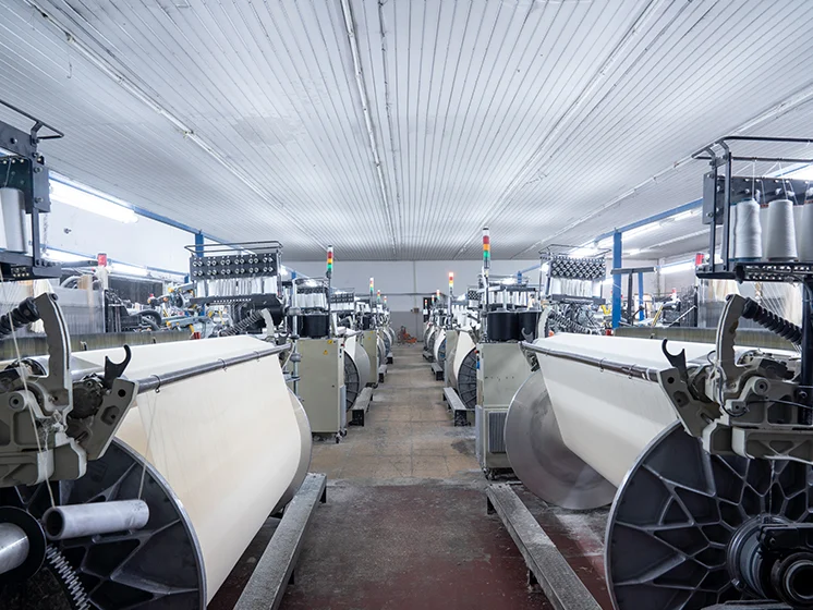 Textile manufacturing facility with rows of automated fabric weaving machines and industrial equipment.