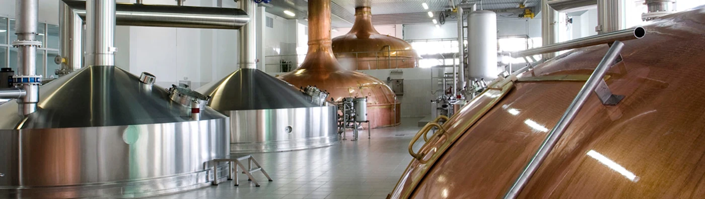 Interior of a brewery with large stainless steel and copper fermentation tanks and equipment.