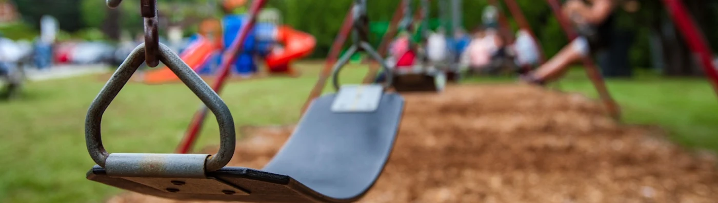 Closeup picture of a swing in a park for kids. Kids swinging in the blurry background.