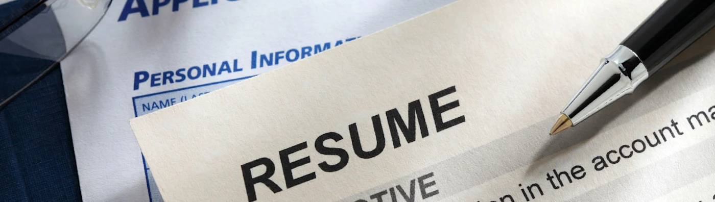 Close up of a resume and job application form with a pen resting on top.
