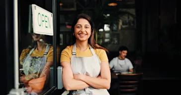 A smiling business owner stands next to her cafe’s open door