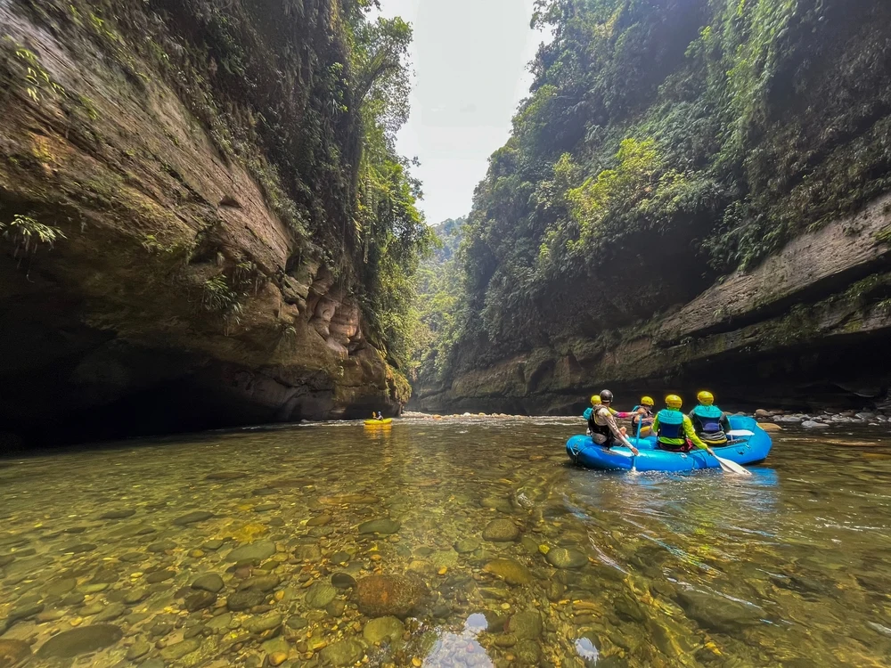 People in an inflatable blue raft paddle down a river.