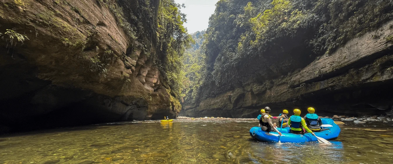 People in an inflatable blue raft paddle down a river.