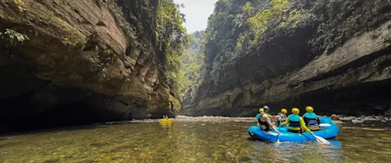 People in an inflatable blue raft paddle down a river.