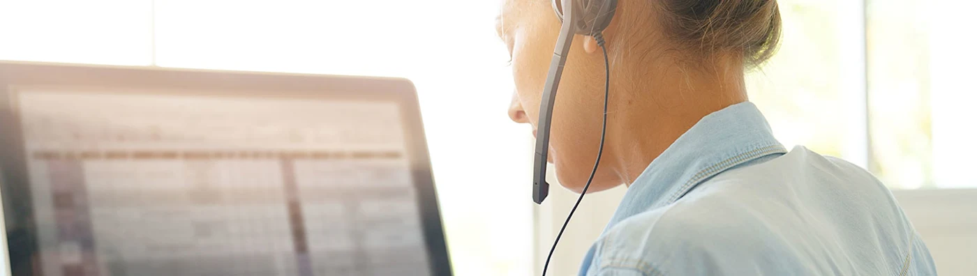 Customer service agent wearing a headset and working at a computer in a bright office.
