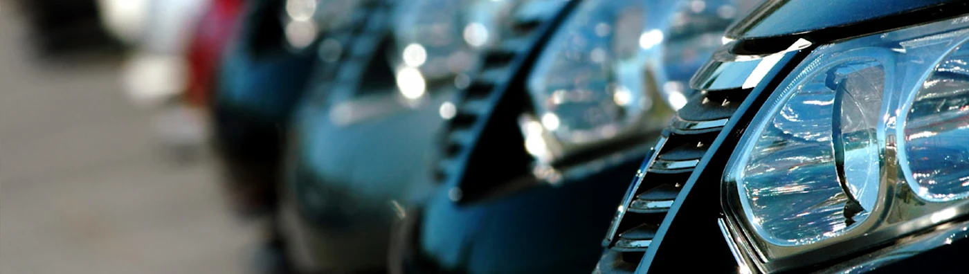 Close-up of parked rental cars in a row, highlighting shiny headlights and grills.