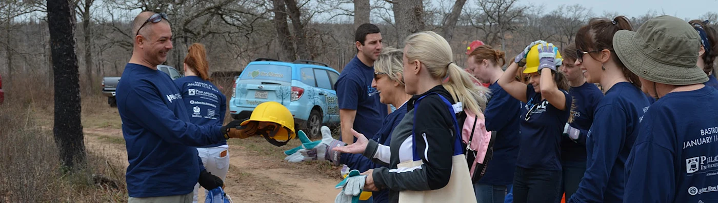 Volunteers prepare for a tree-planting event, putting on gloves and hard hats outdoors.