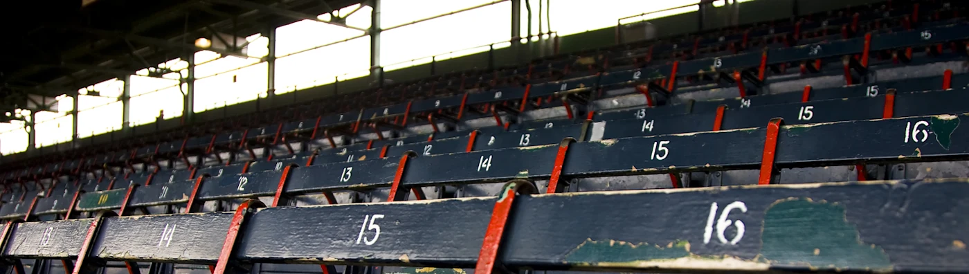 Empty, weathered stadium seats in rows, numbered in white with red supports and peeling paint.