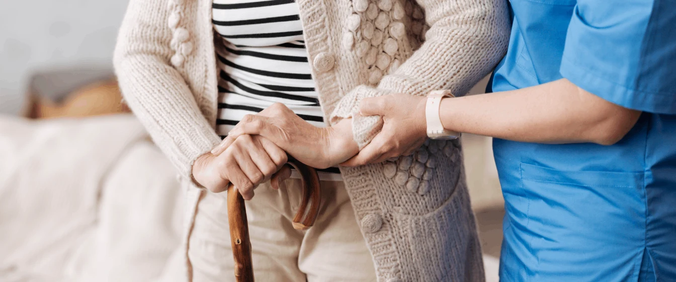 A home health care aide helps a senior stand.
