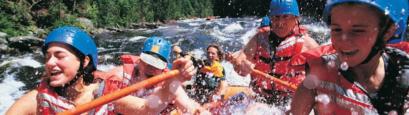 Close up image of a group of people wearing helmets and life vests whitewater rafting through a river.