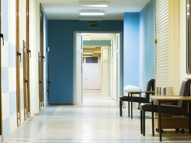Empty hallway in a rehabilitation facility, with open doors and chairs placed along the walls.