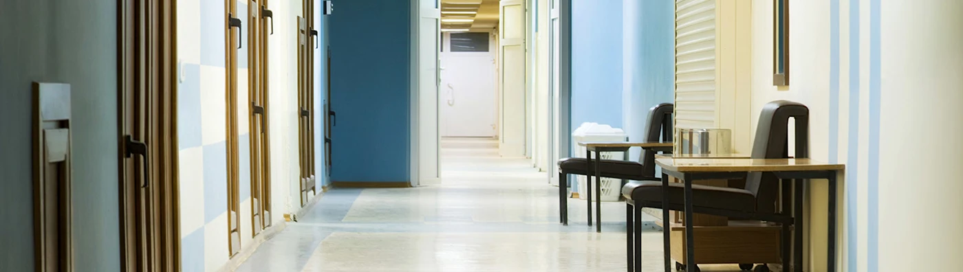 Empty hallway in a rehabilitation facility, with open doors and chairs placed along the walls.