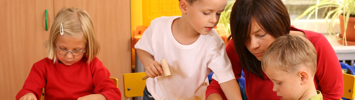 Teacher assists young children with a classroom activity in a bright, colorful setting.