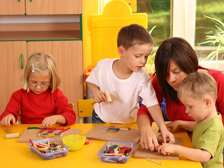 Teacher assists young children with a classroom activity in a bright, colorful setting.