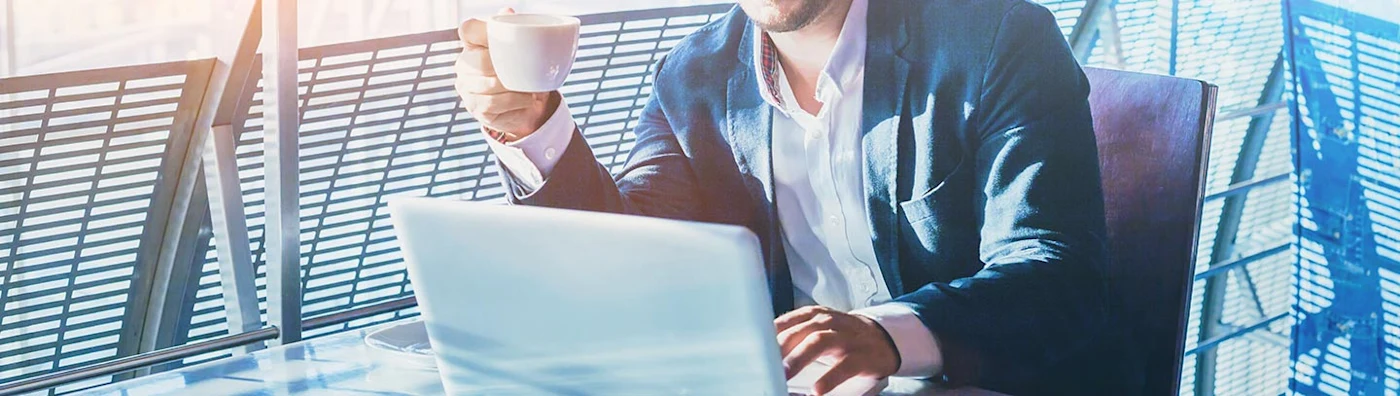 Man drinks a cup of coffee while reading something on his laptop